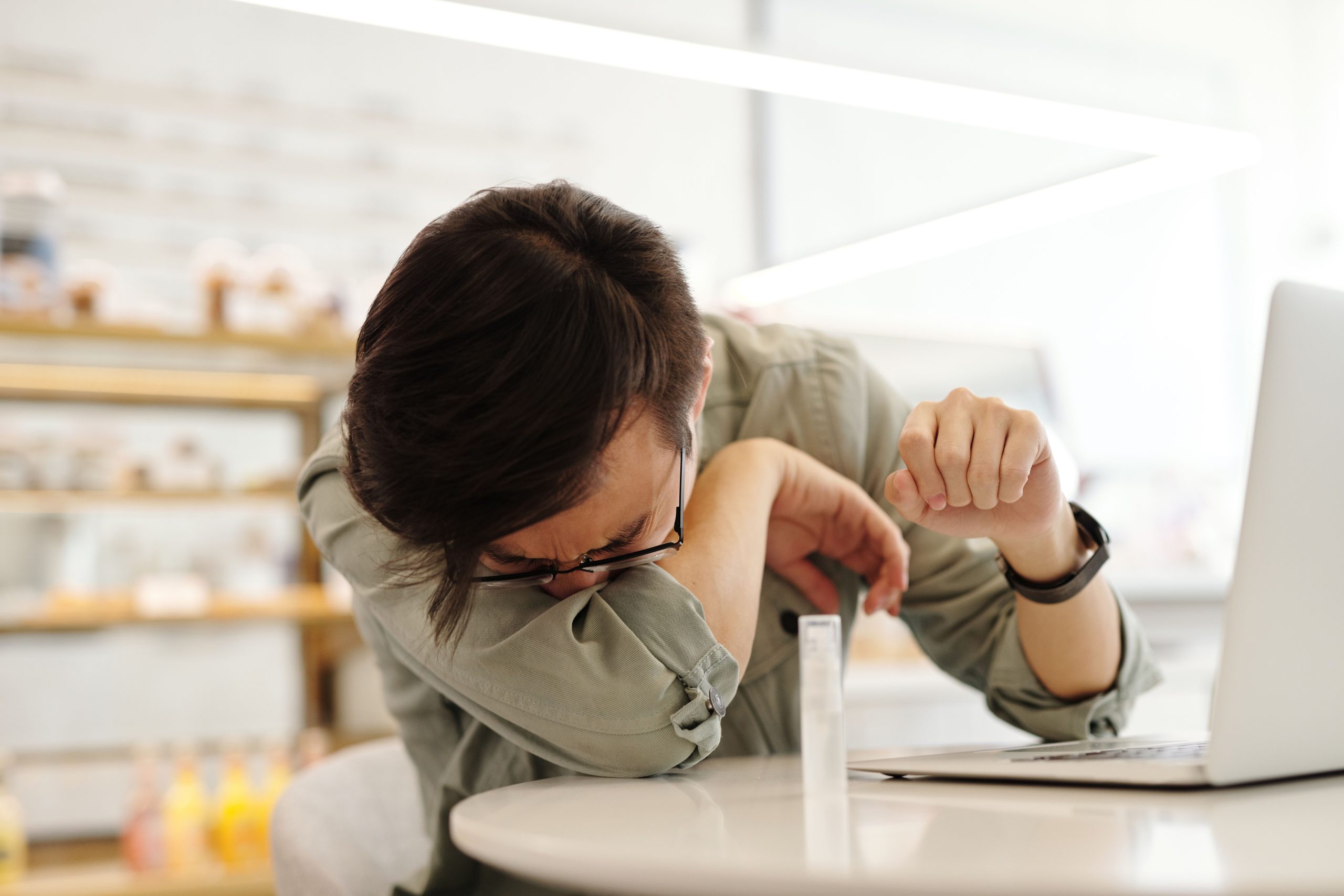 Homme éternuant dans son bras au café