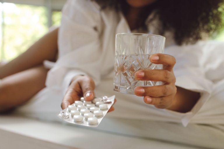 Femme tenant un verre d'eau et son médicament